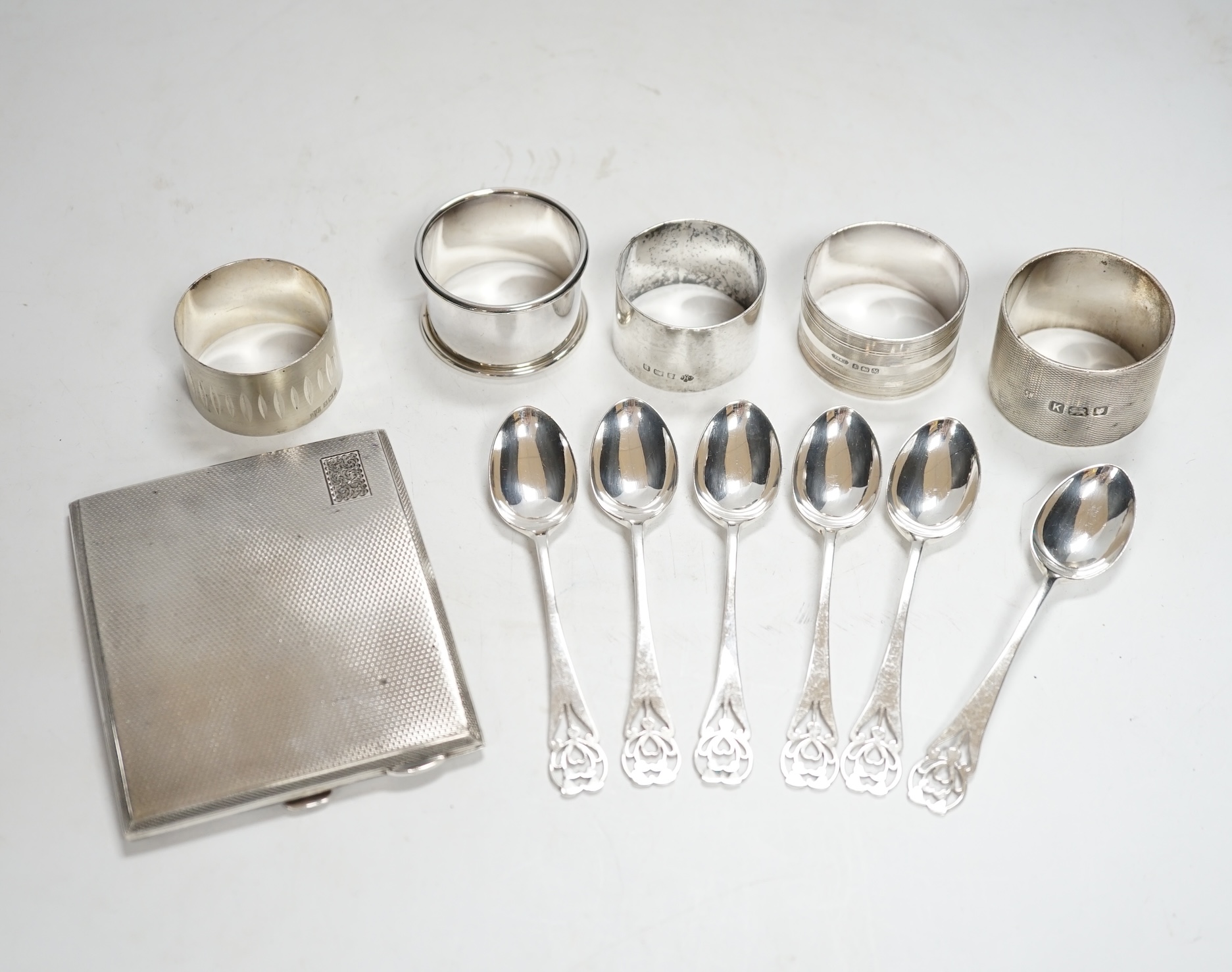 A concave engine turned cigarette case, 10.3cm, five assorted silver napkin rings and a set of six silver coffee spoons, 12.9oz.
